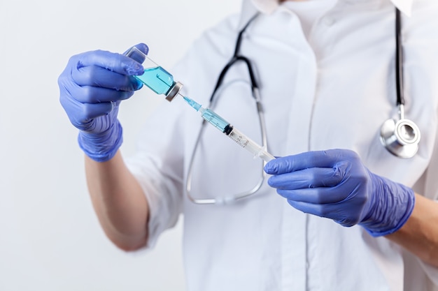 Closeup nurse hand in gloves holds and fills syringe from bottle with vaccine