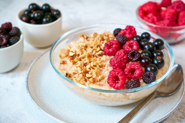 Closeup oatmeal with different berries and crushed nuts in a glass bowl healthy balanced food