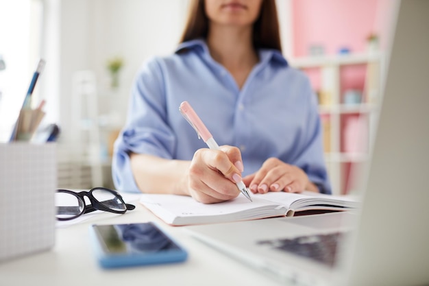 Closeup of office woman sitting at table and making notes in organizer while working on marketing st