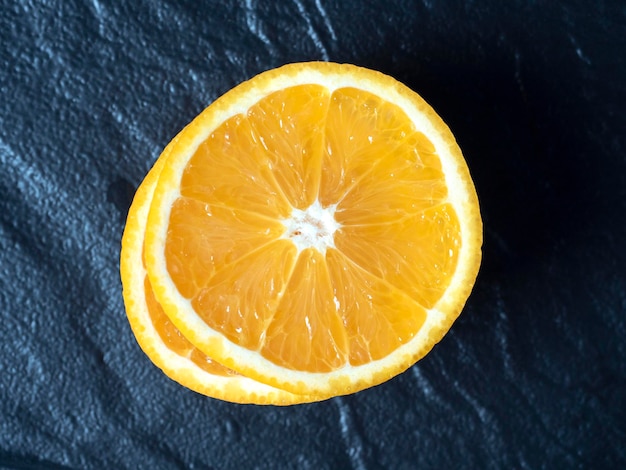 A closeup of an orange cut into slices lies on a dark textured plate Delicious beautiful fruit full of vitamins Top view flat lay