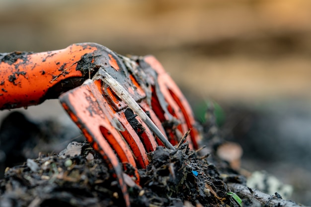 Closeup orange rake on pile of dirty plastic waste on blurred background. Beach environmental pollution concept Clean up rubbish on beach. Ocean garbage. Coast polluted.