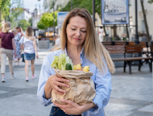 A closeup paper bag with vegetables and fruits in female hands