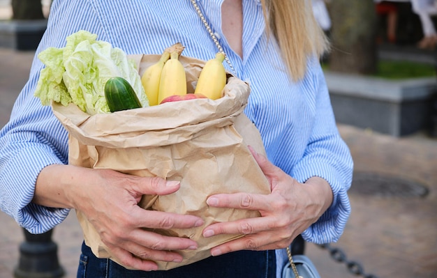 A closeup paper bag with vegetables and fruits in female hands