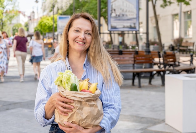 A closeup paper bag with vegetables and fruits in female hands