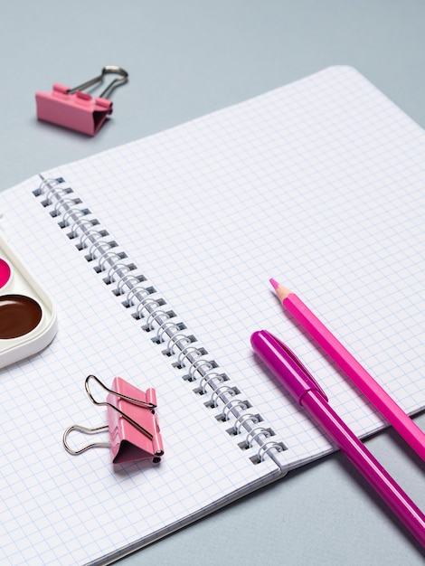 Closeup of a paper notebook with blank sheets a pen a pencil and a paper clip on a blue background