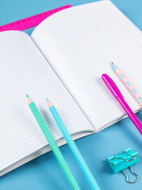 Closeup of a paper notebook with blank sheets a pen a pencil and a paper clip on a blue background