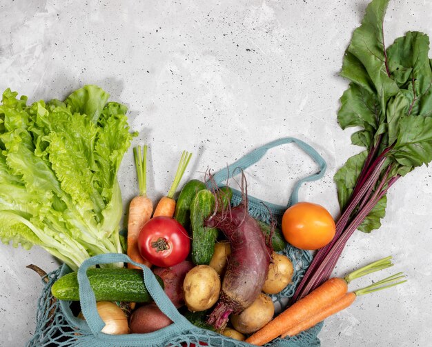 Closeup part of string bag with fresh farm vegetables on grey concrete background