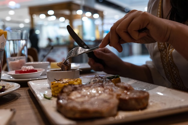 Closeup partial view of woman enjoy eating steak with fork and knife in restaurant