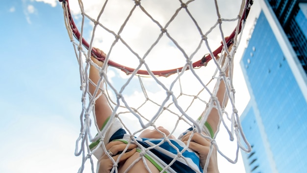 Closeup photo of active 3 years old toddler boy holding on basketball net ring. Concept of active and sporty children. Health of new generation kids