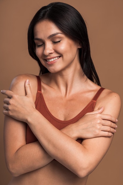 Closeup photo of attractive charming lady smiling with closed eyes, hold herself hugging shoulders with pleasant feeling , isolated on beige color background