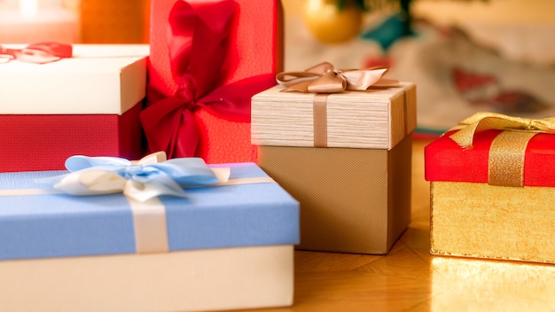 Closeup photo of beautiful boxes for gifts or presents with ribbons and bows lying on wooden floor at living room. Perfect abstract background for holidays or celebrations