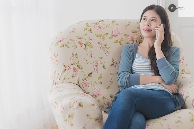 closeup photo of beautiful elegant woman sitting on sofa chair and looking window view using mobile smartphone working at home.