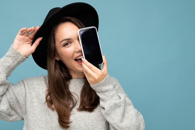 Closeup photo of beautiful positive woman person wearing black hat and grey sweater holding