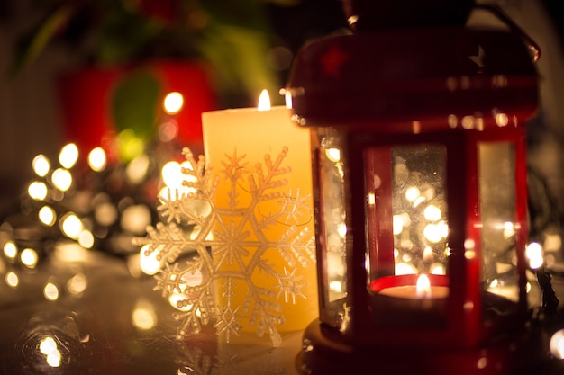 Closeup photo of Christmas lights, burning candle and vintage lantern on table