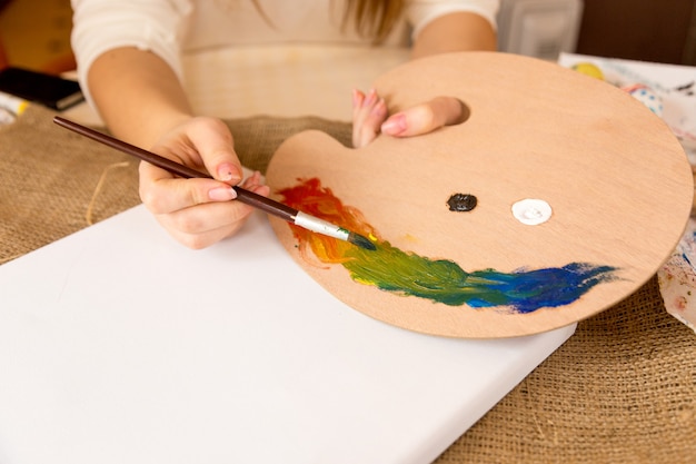 Closeup photo of female artist mixing oil paints on wooden pallet