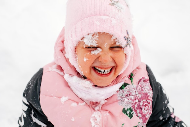 Closeup photo of female russian kid smiling with teeth with face covered with snow with eyes closed ...