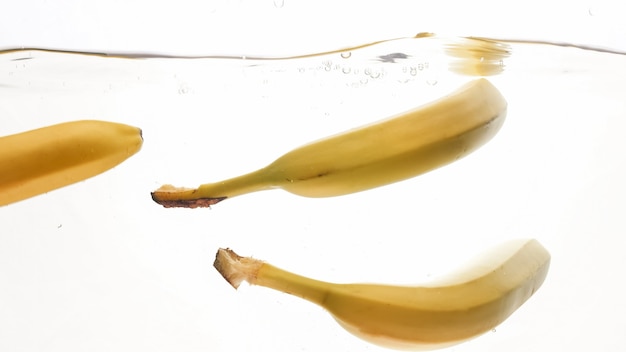 Closeup photo of fresh ripe yellow bananas falling and splashing in clear water against isolated white backgorund