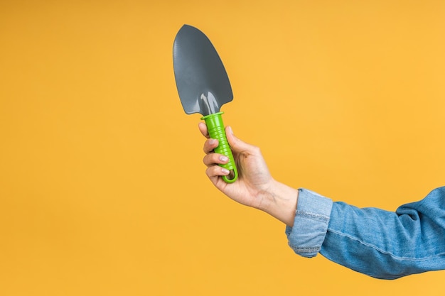 Photo closeup photo of green shovel in woman's hand isolated over yellow background