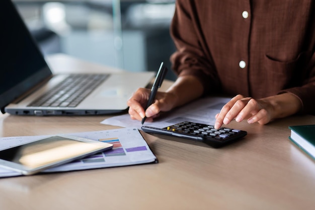 Closeup photo hands of a young woman in a brown shirt calculating on a calculator and writing