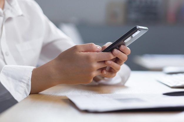 Closeup photo the hands of a young woman in a white shirt are holding a mobile phone typing a