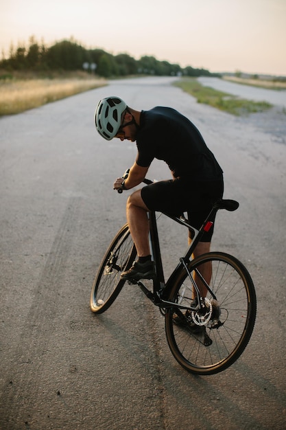 Closeup photo of a man dressed in cycling clothes starting riding a modern bicycle on the asphalt outoftown bicycle path Active sporty people concept image