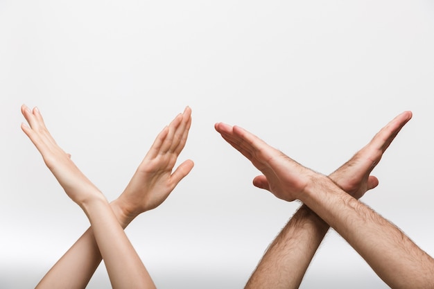 Closeup photo of a man's and woman's hands isolated over white wall wall showing stop gesture.