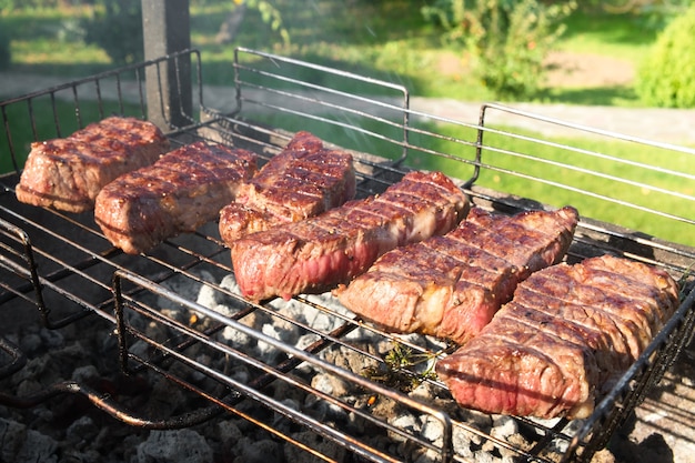 Closeup photo of medium grilled meat on a wire rack. Steaks barbecue on a brazier with natural smoke. Outdoor cooking.