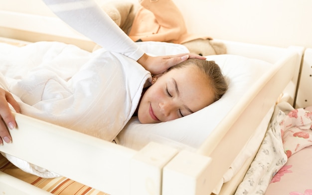 Closeup photo of mother caressing sleeping daughter at bed