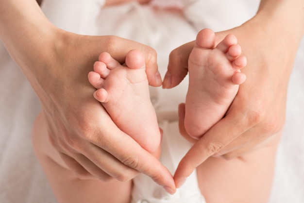 Closeup photo of mother's hands holding newborn's small feet and making heart with fingers on isolated white cloth background