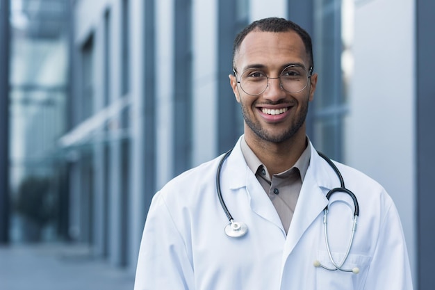 Closeup photo portrait of young african american doctor outside hospital man in medical coat smiling