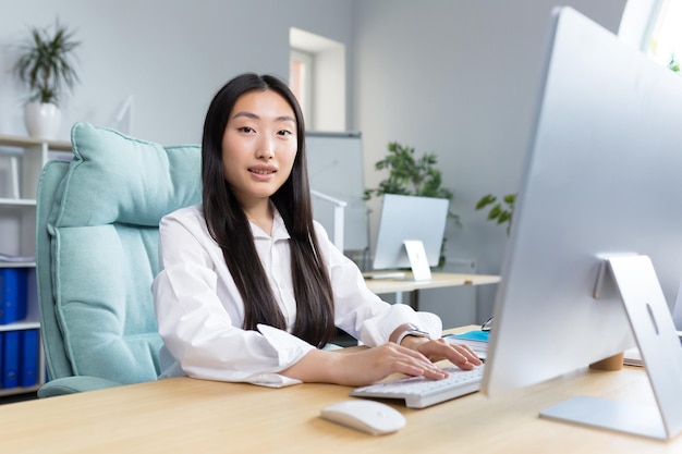 Closeup photo portrait of a young beautiful asian woman secretary sitting at the desk at the