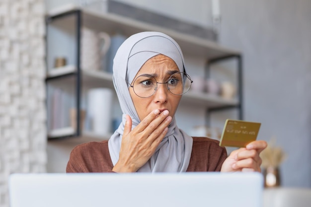 Closeup photo portrait of a young muslim woman in a hijab sitting at home using a laptop and holding