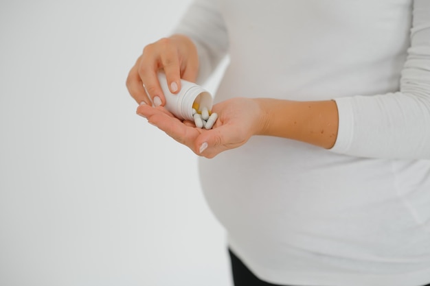 Closeup photo of pregnant woman holding pills and medicine bottle