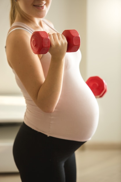 Closeup photo of pregnant woman lifting dumbbells