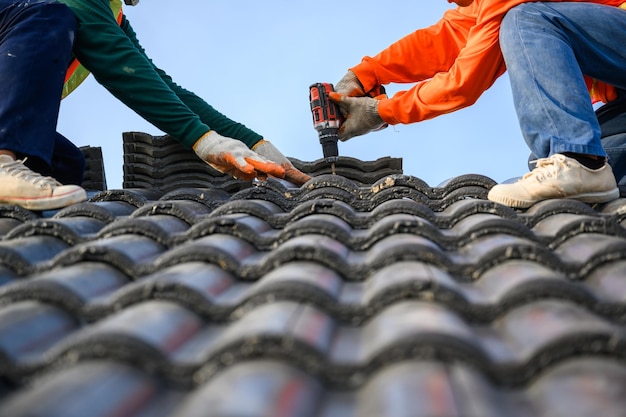 Closeup photo of a roofer working on the roof of the house Use a drill to drill the screws to fix the cement tile roof