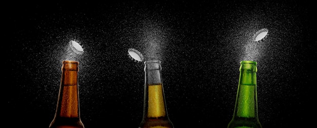 Closeup photo of an three beer bottle splashing beer drops on a black background Beer cap flying on top of the bottle