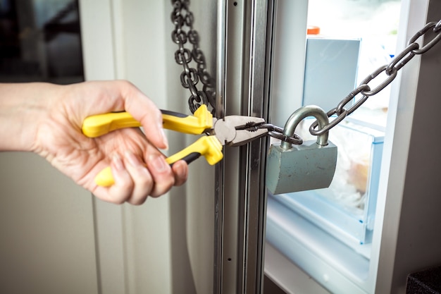 Closeup photo of woman cutting chain on fridge with pliers