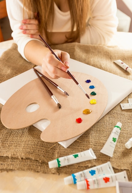 Closeup photo of young female artist sitting at table and drawing on canvas