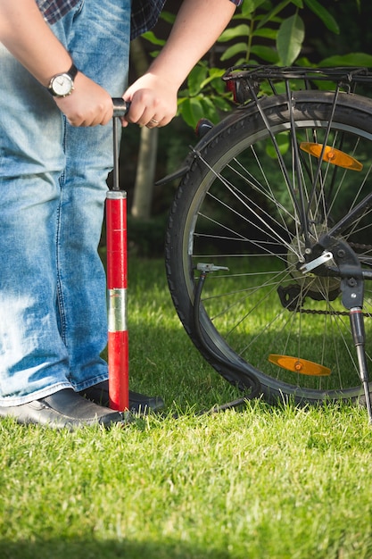 Closeup photo of young man pumping bicycle wheel on grass