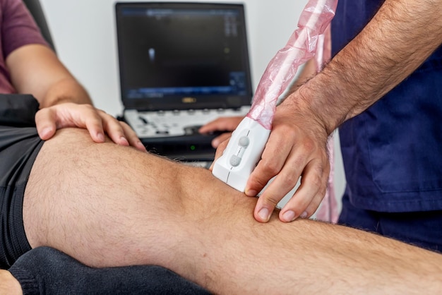 Closeup of a physiotherapist performing an ultrasound of the knee on a patient lying on a stretcher