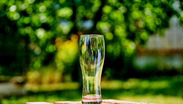 Closeup picture of an ampty beer glass on a brown wooden table Sun shines through the glass Blurred green nature background