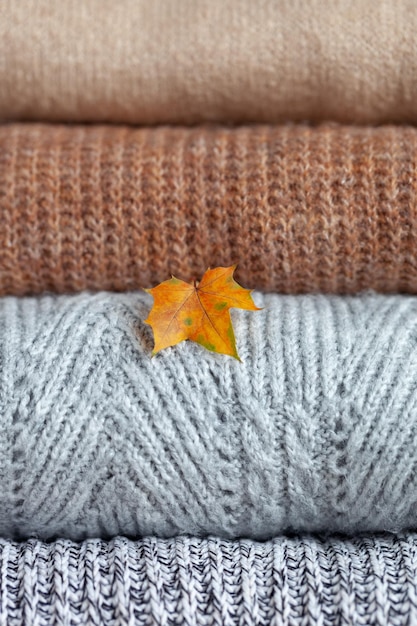 Closeup Pile of cozy knitted sweaters with yellow maple leaf on a neutral background Warm concept