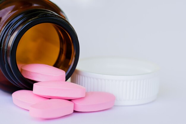 Closeup pink pills from bottle on white background  