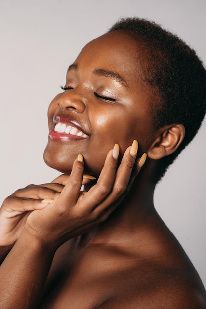 Closeup portrait of an afro woman smiling with closed eyes and touching perfect skin of cheek agains