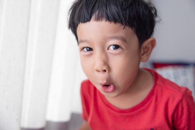 Closeup portrait Asian child boy straight black hair wearing a red shirt looking at camera