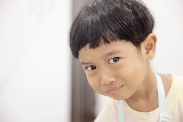 Closeup portrait Asian child boy straight black hair wearing a white shirt looking at camera