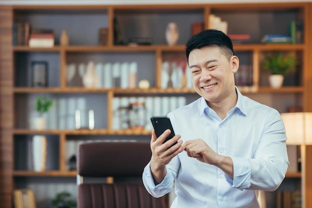 Closeup portrait of Asian man working in classic home office Businessman using phone looking at smartphone screen and smiling