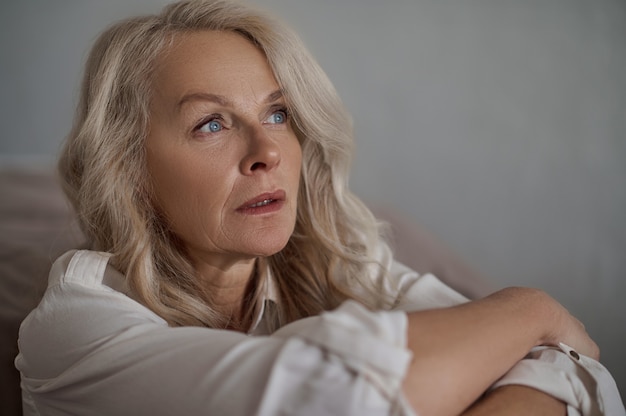 Closeup portrait of an attractive blue-eyed mature sad lady with a faraway look looking away