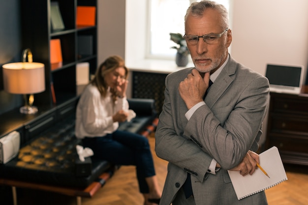 Closeup portrait of an attractive serious psychologist thinking while holding a notepad and pencil in his hand