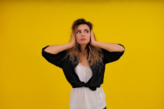 Closeup portrait of a beautiful girl on a yellow background the woman covered her ears with her hands human emotions